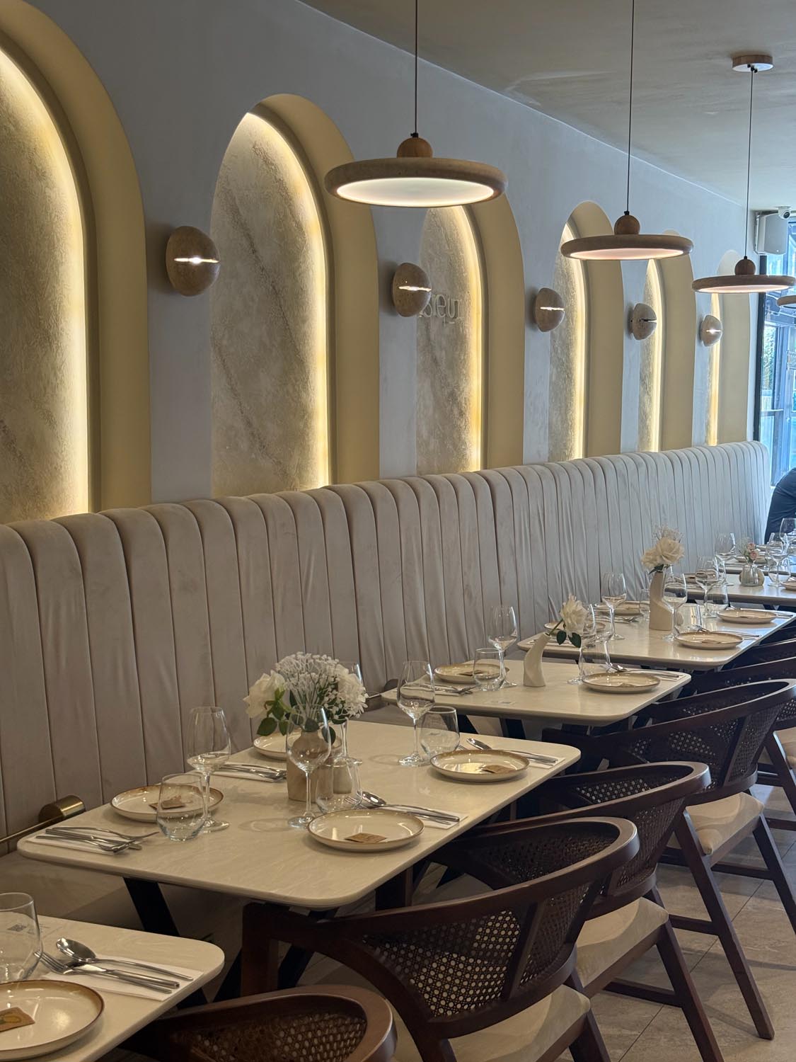 Row of backlit arches above the banquette seating with fresh white flowers on each table