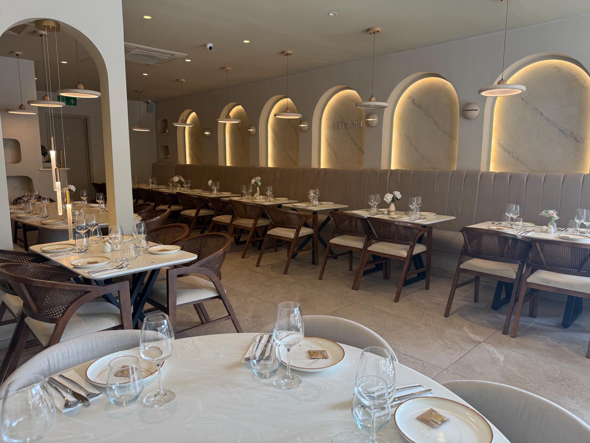 Wide view of the Monsieur dining room, illuminated marble arches above a channelled banquette with laid tables