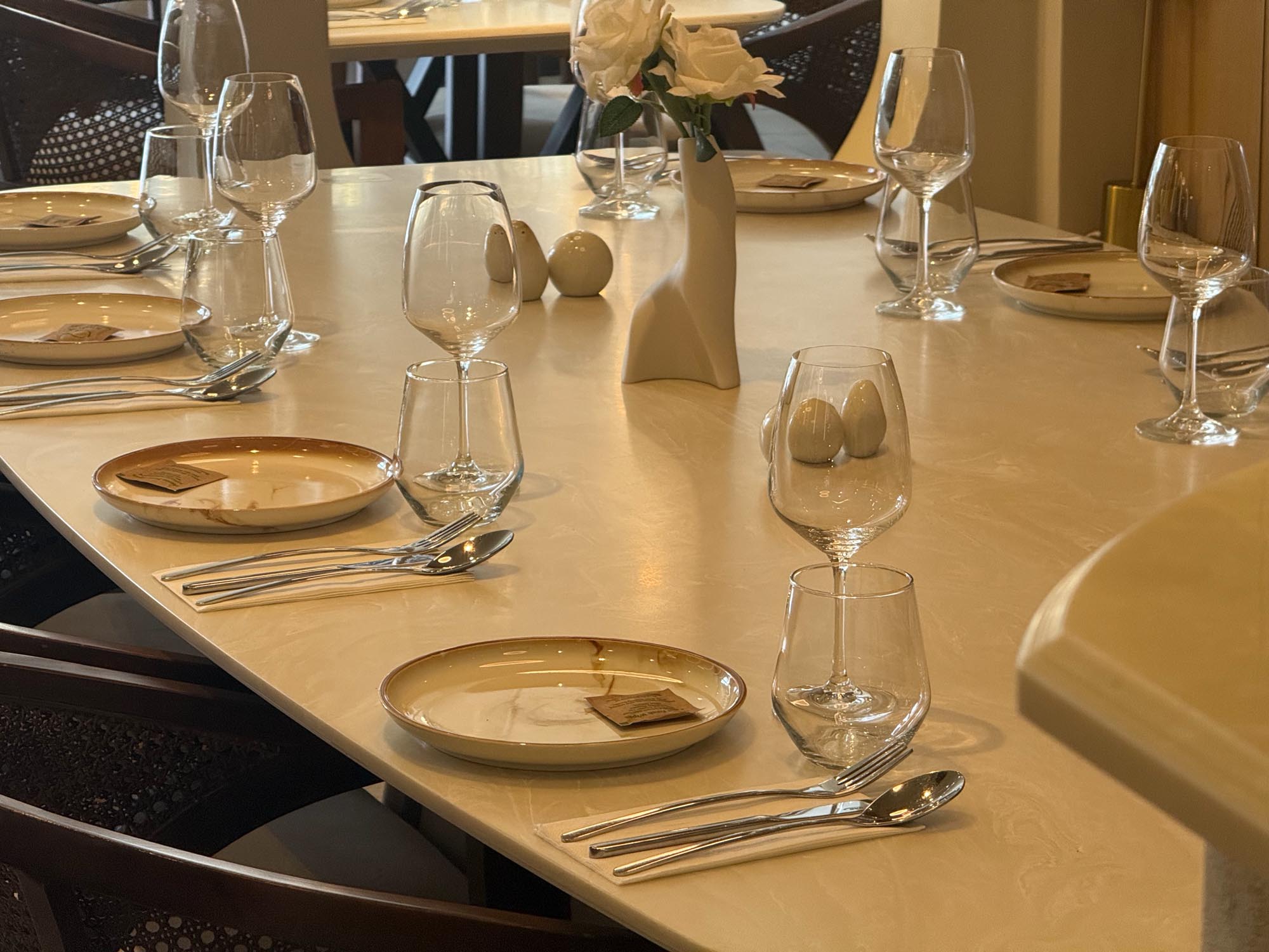 Close-up of a Monsieur place setting: rimmed ceramic plate, polished cutlery and glassware on a cream marble table