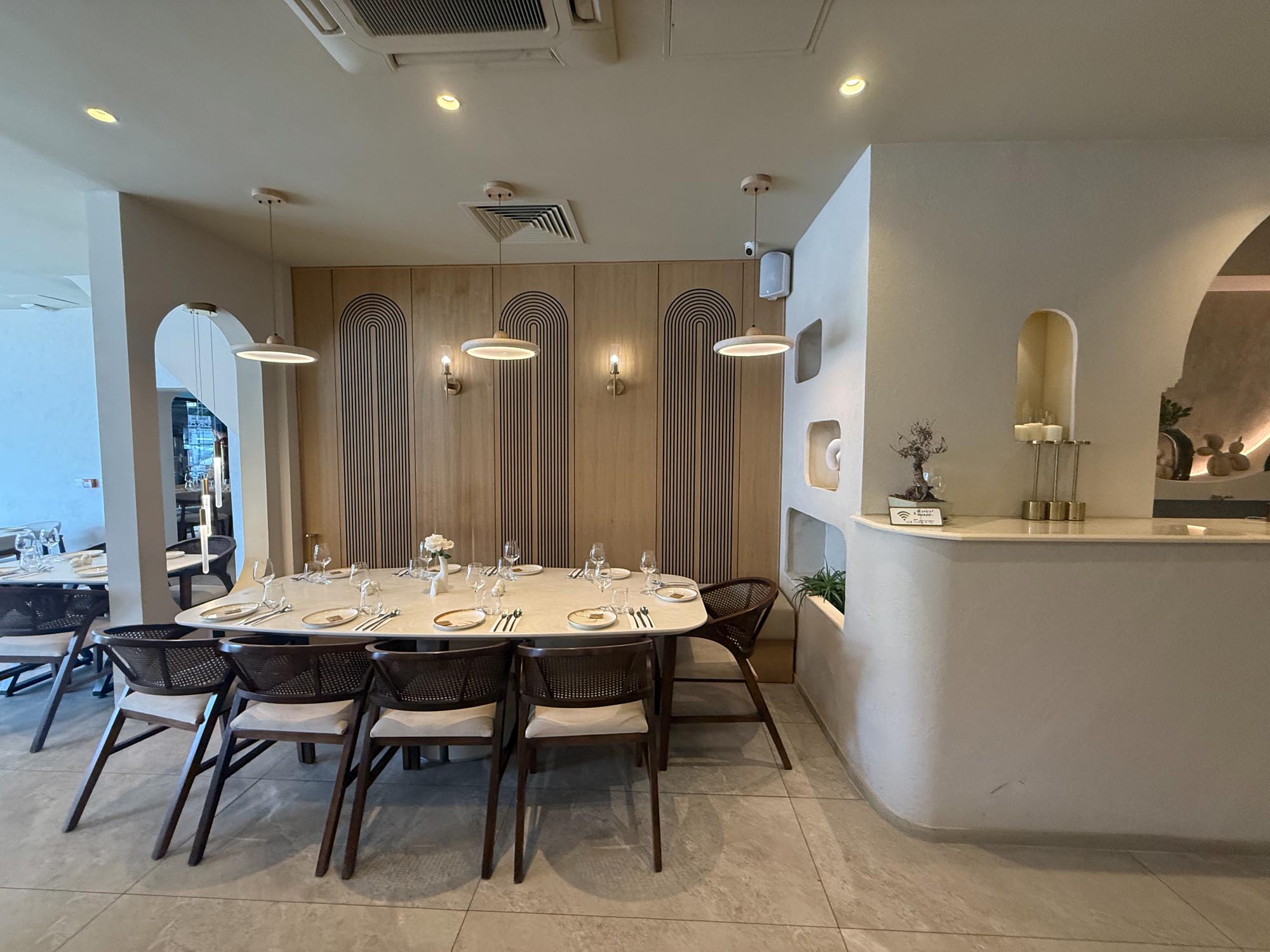 Curved plaster host counter with candles and a bonsai beside an oval table for eight