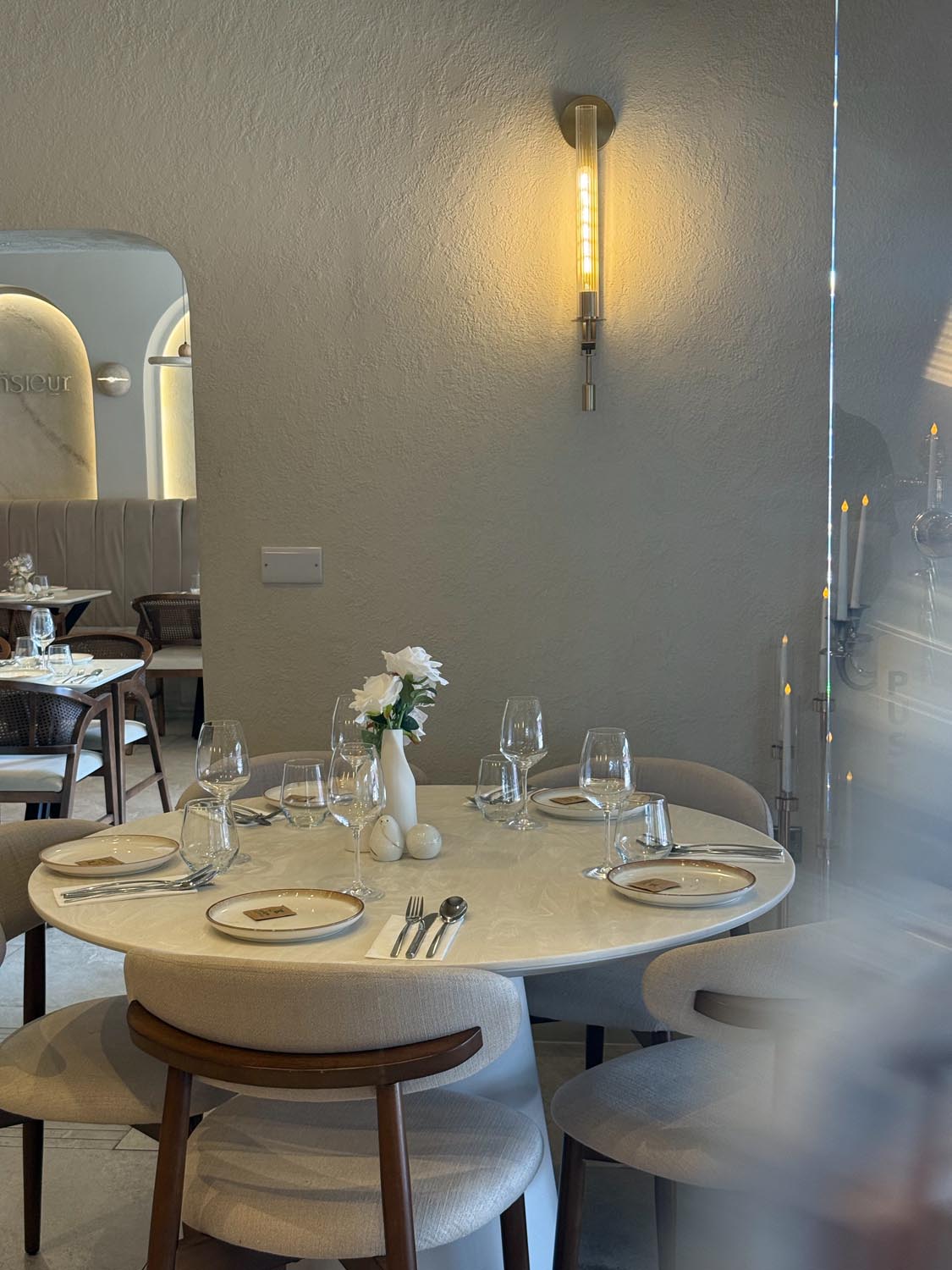 Round marble table set for four beneath a slim brass wall light in a quiet corner of the restaurant