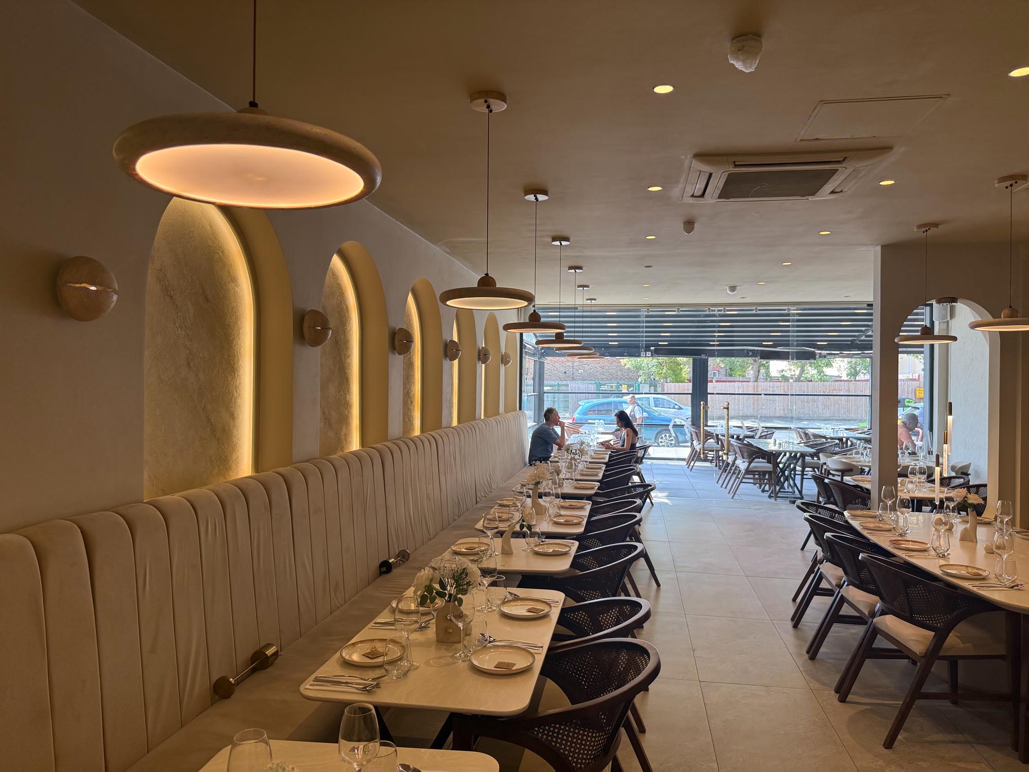 Monsieur dining room with backlit plaster arches, a long cream banquette and pendant lights leading to the street frontage